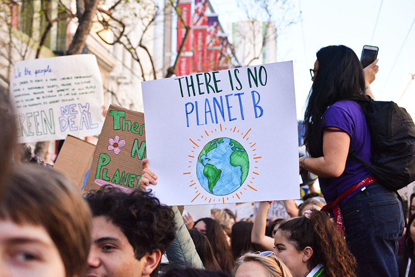 Menschen auf einer Demonstration, die verschiedene Schilder hochhalten. Im Mittelpunk steht eines mit der Aufschrift: "There is no Planet B" (Es gibt keinen Planeten B)