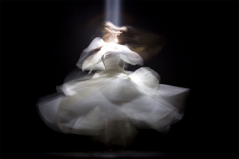 Schleierhaft Figur, die eine Seele darstellen soll. Weißes Kleid, mit einem Lichtstrahl von oben auf schwarzem Hintergrund.