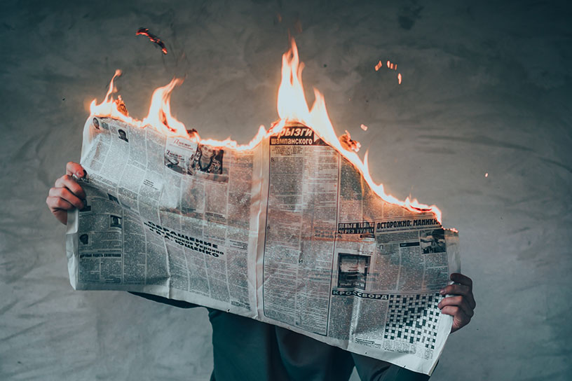 Mensch mit einer brennenden Zeitung in der Hand.