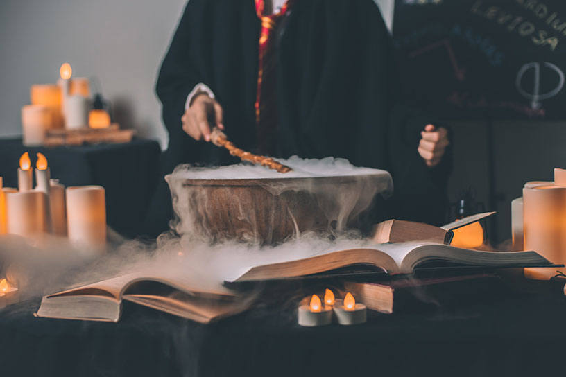 Ein Harry Potter Kittel, mit Zauberstab über eine dampfenden Schüssel, umgeben von Kerzen. 