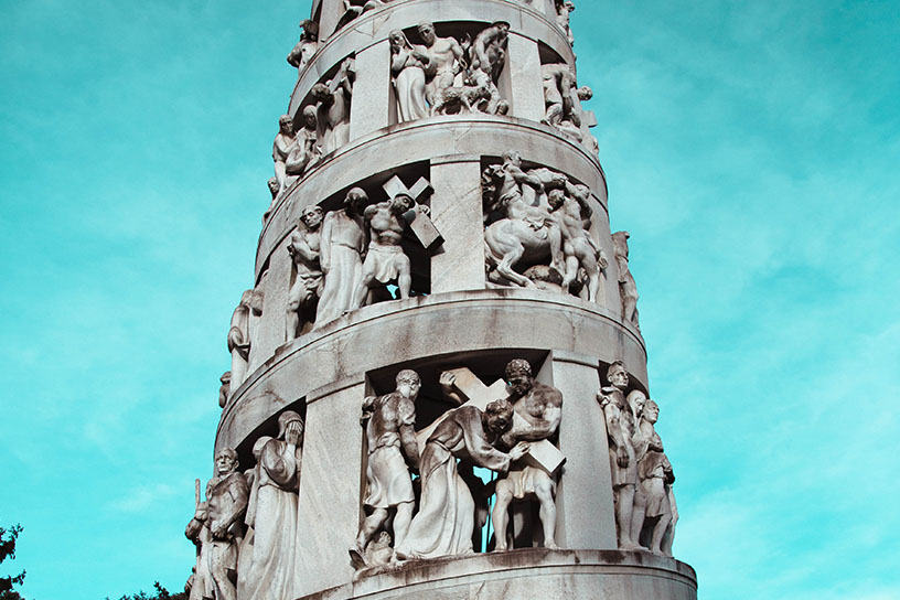Ein Turm aus Stein. Zwischen den Säulen sind Menschen, die den Turm mit stützen. 