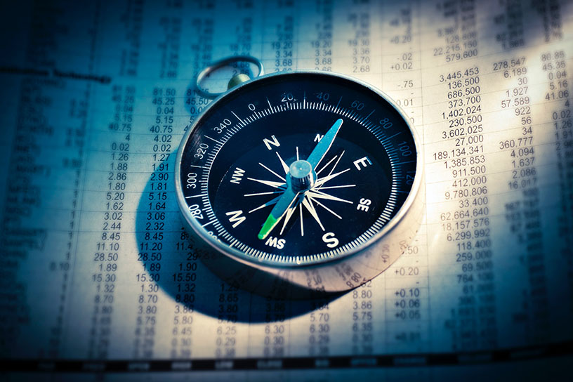 Ein Kompas auf einem Blatt Papier, welches Börsen Kurse dokumentiert. 